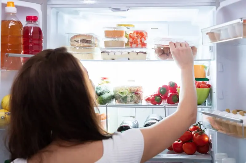 open fridge door with containers with pre-chopped food and woman reaching in