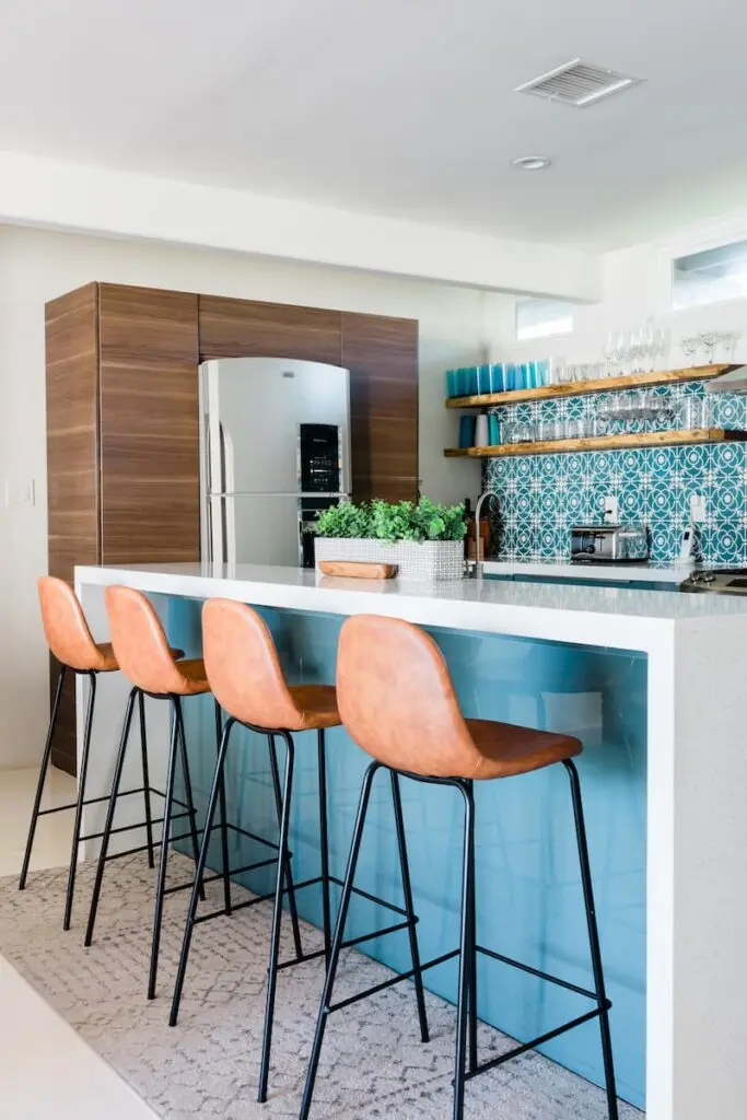 Popular color trend dopamine decor seen here with pink bar stools, white island and white and blue wallpaper